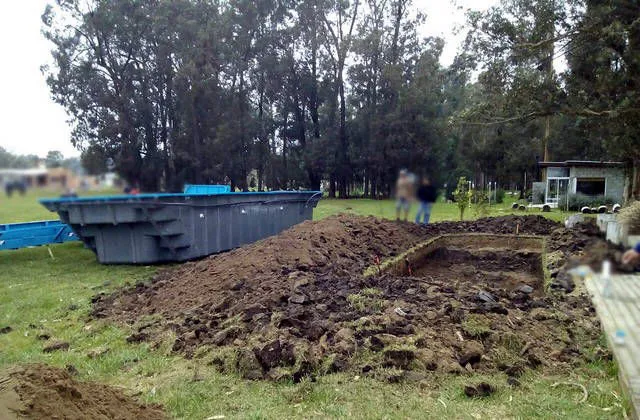 Pozo recién excavado en un terreno con césped; al costado espera el casco de la pileta de fibra de vidrio