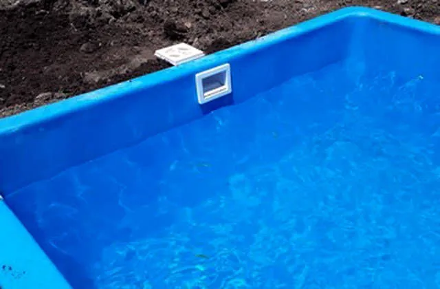 Pileta de fibra de vidrio llena de agua con el skimmer colocado, todavía con tierra alrededor
