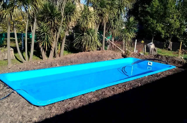Pileta de fibra de vidrio llena de agua, con el terreno sin terminar alrededor y palmeras al fondo