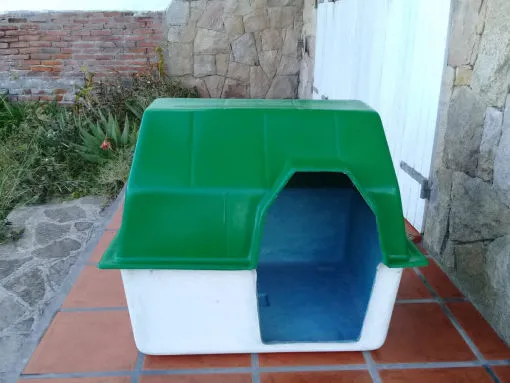 Cucha de fibra de vidrio blanca con techo verde, vista de frente, sobre un patio de baldosas